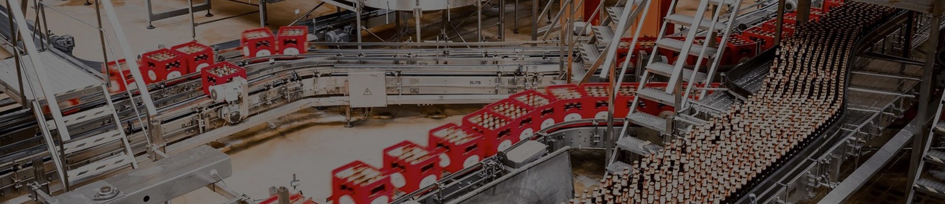 A conveyor system in a production facility transporting red crates filled with bottles, with interconnected metal tracks and machinery creating a seamless assembly line.