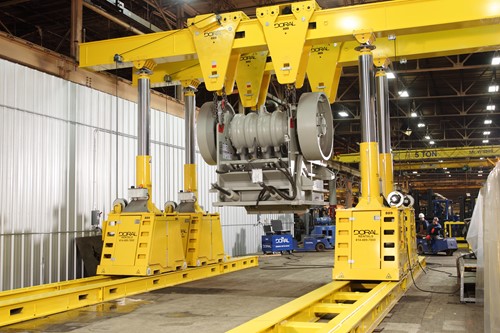A bright yellow Enerpac gantry system is used to transport a large piece of rock-crushing equipment inside an industrial facility, with precision rigging and support structures visible in the background.