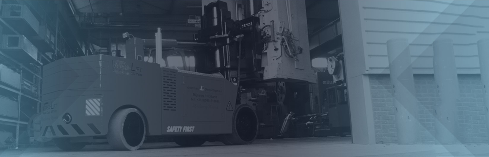 A large industrial forklift labeled “Versa-Lift” inside a warehouse, positioned next to a heavy piece of equipment, with a clean and structured industrial environment in the background.