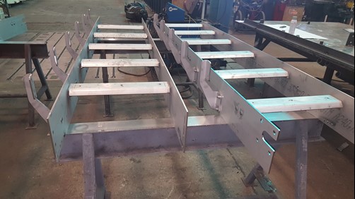 A stainless steel conveyor frame under construction, featuring side guards and support brackets, designed for a meat processing operation.