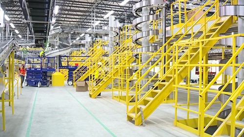 A warehouse with yellow staircases and platforms leading to silver spiral conveyors, surrounded by industrial equipment and a clean, organized workspace.
