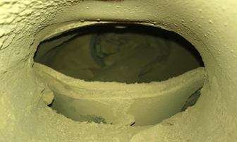A close-up view of an industrial pipe or duct interior coated with a thick layer of yellowish material, possibly residue or buildup, indicating industrial or manufacturing processes.