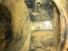 The interior of a pipe or duct showing metal plates fastened with bolts, surrounded by dirt and residue, likely part of an industrial or repair process.